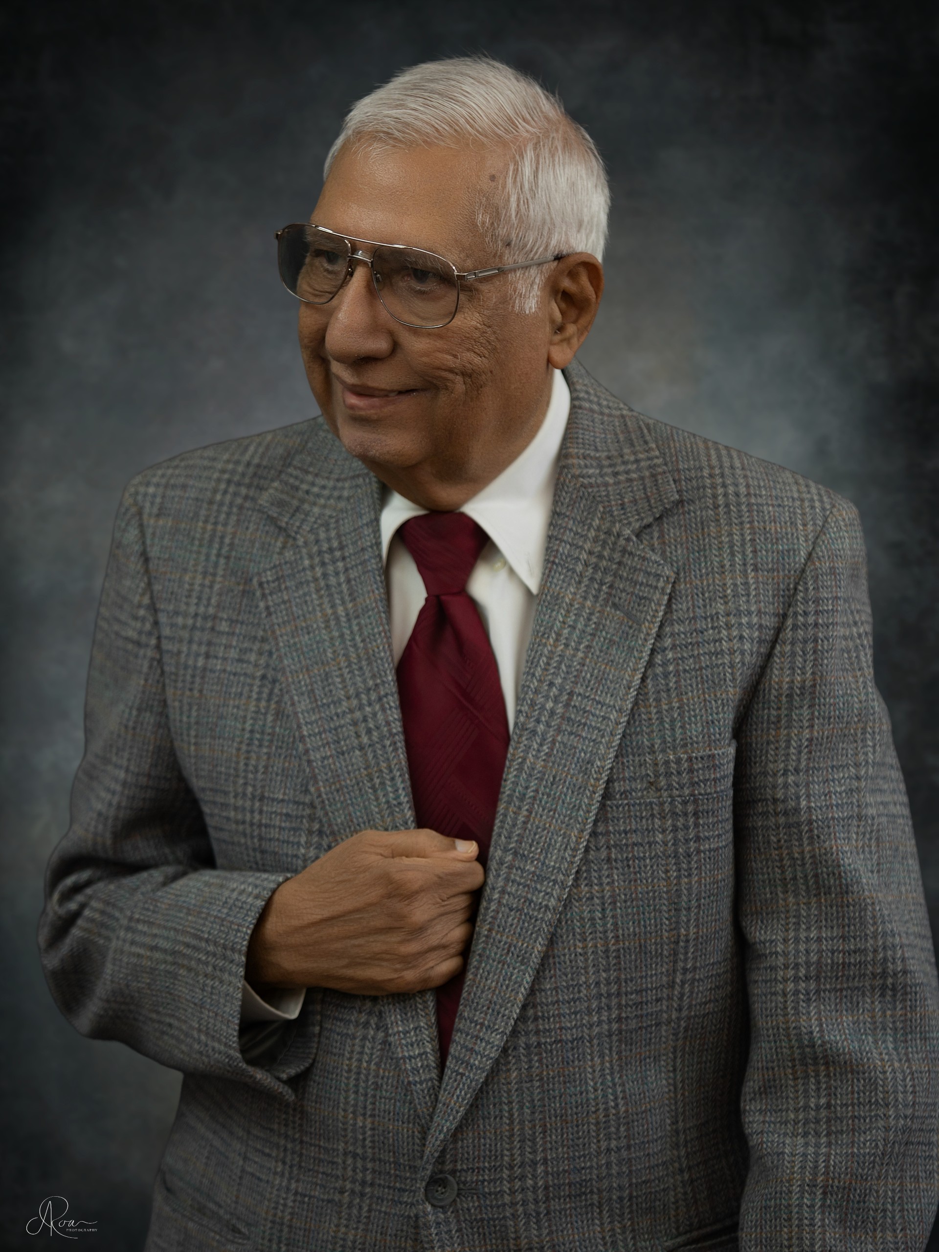 Portrait of a distinguished-looking older man wearing a grey suit and smiling.