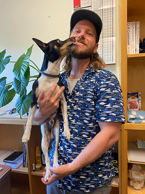 A young man holds a small dog, who is reaching up with his nose to the man's face.