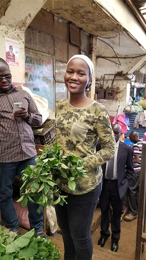 A young woman holds a basket of greens in an urban setting.