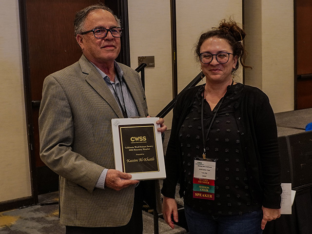 Two people stand together holding an award plaque in a conference setting.