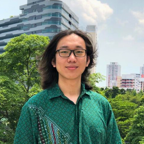 Man in green shirt stands in front of building and trees