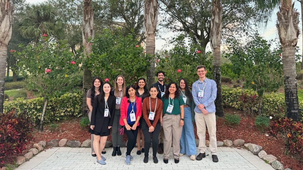 A group of young people standing on a patio with tropical trees in the background.