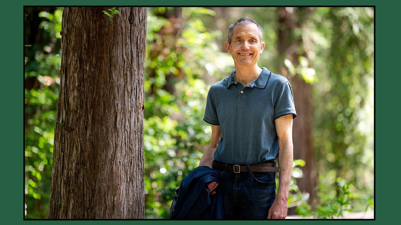 Man standing by a redwood tree, with forest behind him