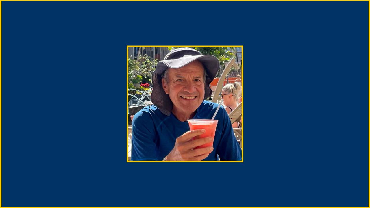 Older man smiling and holding a beverage.