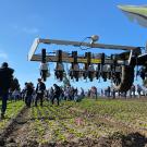 We're looking from underneath a large, tractor-like machine with a metal arm extended to one side. It has little nozzles on it, pointing downward.