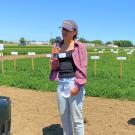 Woman stands with microphone in front of field. Man holds up banner besides her. 