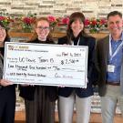 Three women hold a giant check and smile. The check is for 2,500 dollars.Two men flank them.